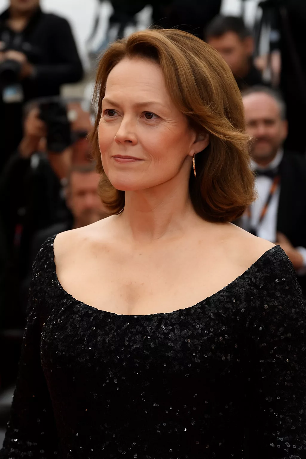 Silhouette féminine élégante sur un tapis rouge, mise en lumière par des projecteurs cinématographiques, ambiance glamour rappelant l’univers de Sigourney Weaver sans montrer son visage.